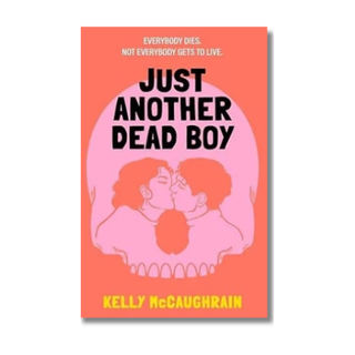 Book cover for 'Just Another Dead Boy' by Kelly McCaughrain, featuring a coral pink background, a large pale pink skull, two kissing figures inside the skull, and bold black title text with yellow author text.