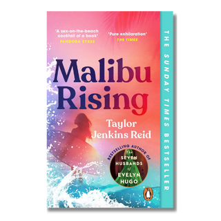 The front cover of the book Malibu Rising by Taylor Jenkins Reid, featuring a vibrant sunset gradient background with ocean waves and a silhouette of a woman on a surfboard. A vertical teal spine band on the right reads 'THE SUNDAY TIMES BESTSELLER' with the Penguin logo at the bottom.