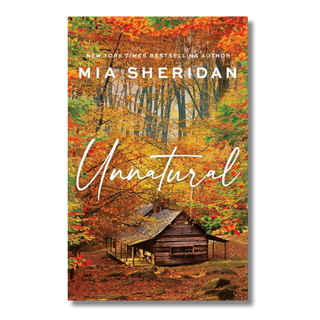 Book cover for 'Unnatural' by Mia Sheridan, featuring an autumn forest scene with colorful fall foliage and a rustic cabin, with the title in large white script across the center.